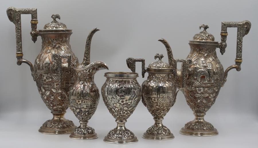 This five-piece Baltimore Silversmiths Mfg Co tea service ($2/3,000) comprises a teapot, coffee pot, creamer, lidded sugar, and open waste vessel. It has ornate repousse decoration.